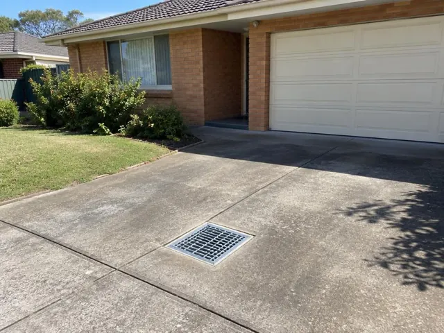 Driveway with a square drain grate beside a brick house and garage in Parklea