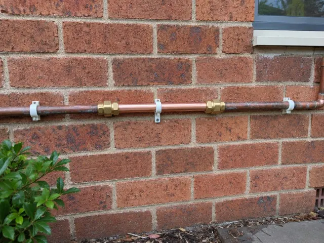 Repaired copper water pipe mounted on a brick exterior wall beside a window in Kings Park