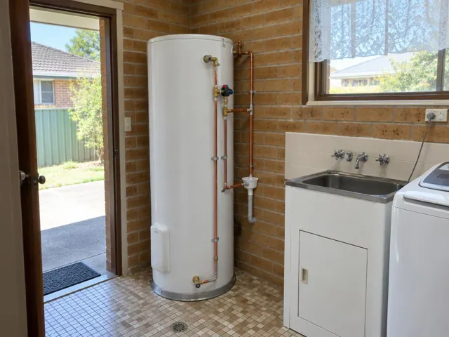 White hot water cylinder in a brick laundry beside a sink and window in Marayong